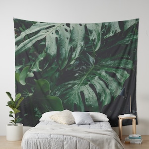 May include: A tapestry featuring a close-up of large, green tropical leaves with water droplets. The leaves have a textured, veined appearance and are arranged in a lush, jungle-like setting.