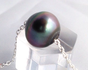 May include: A single, large, dark pearl pendant necklace. The pearl is a deep, iridescent color with hints of green and purple. The chain is a delicate silver color, and the necklace is displayed on a clear, geometric stand.