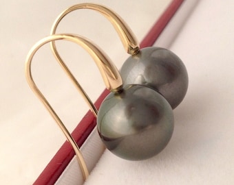 May include: A pair of gold-colored hook earrings with large, dark gray, round pearls. The earrings are displayed against a white background with a red accent.