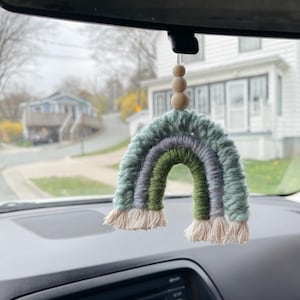 Peut inclure: Un charme de voiture en crochet arc-en-ciel vert, bleu et gris suspendu au rétroviseur d'une voiture. Le charme est fait de fil et a une chaîne de perles en bois.