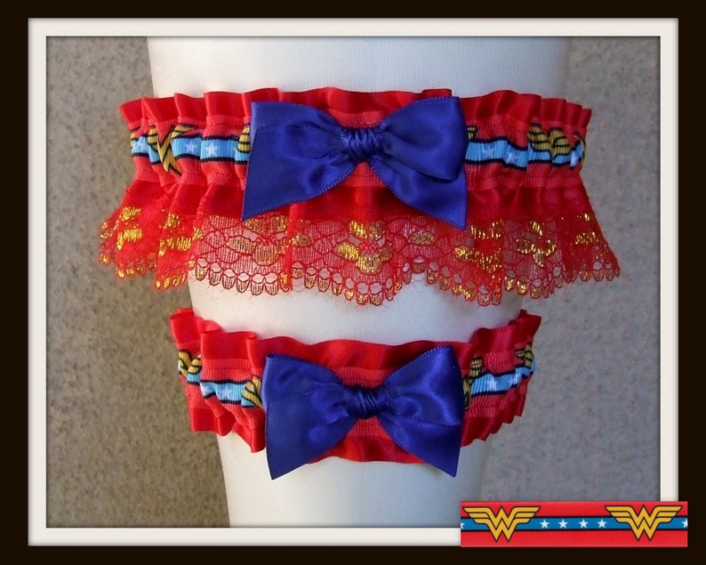 May include: A set of two red elastic garters featuring a blue ribbon with white stars and gold lightning bolt patterns. Each garter is adorned with a deep blue satin bow and a layer of red lace with gold metallic thread accents throughout.