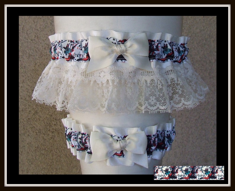 May include: A set of two white garters featuring a patterned fabric with red and teal accents, topped with a solid white satin bow. The larger garter includes a wide layer of intricate white lace trim, while both pieces have a gathered elastic band.