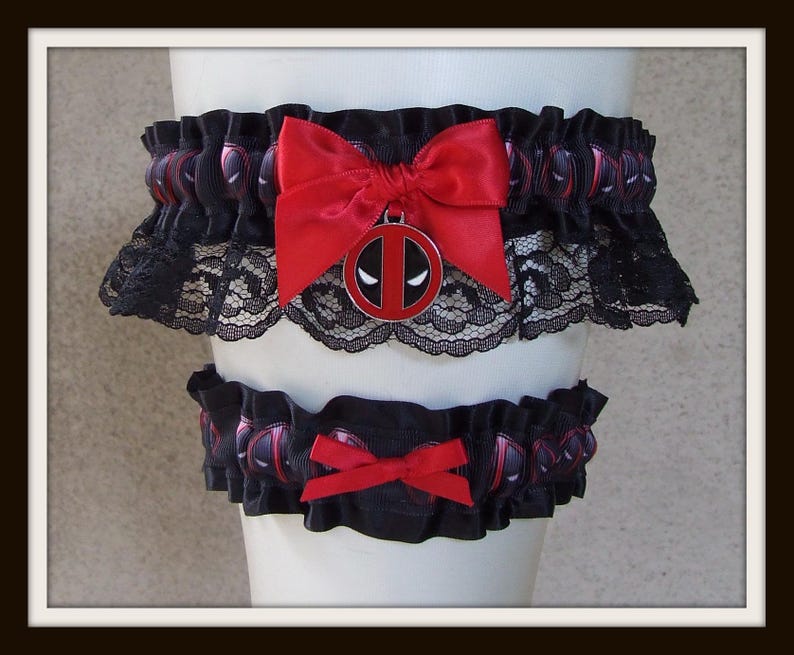 May include: A set of two black elastic garters featuring a repeating Deadpool mask pattern. The larger garter includes a red satin bow and a circular Deadpool logo charm, while the smaller garter features a simple red satin bow accent.