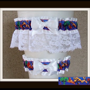 May include: A set of two leg garters featuring a blue ribbon with a colorful comic book superhero print, accented by white satin bows and a wide layer of white floral lace trim. The superhero pattern includes figures like Hulk, Iron Man, and Spider-Man.