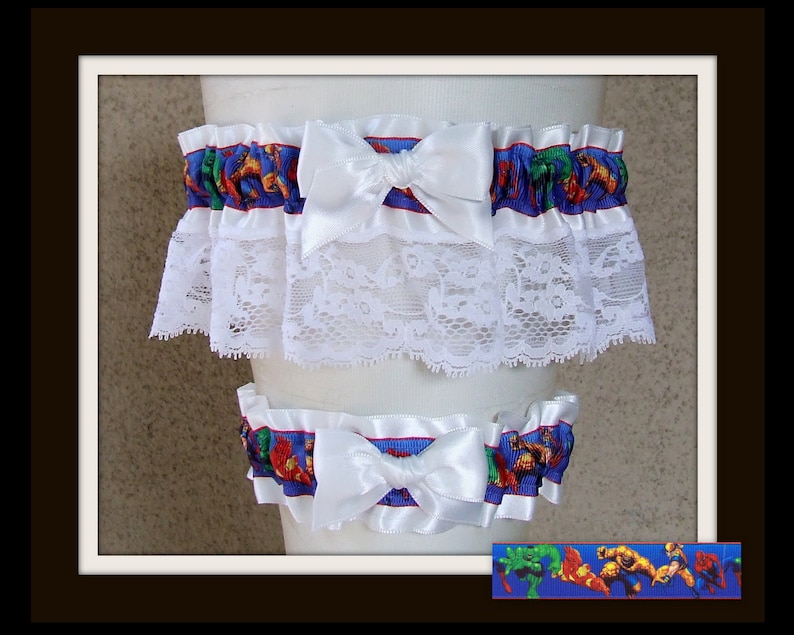 May include: A set of two leg garters featuring a blue ribbon with a colorful comic book superhero print, accented by white satin bows and a wide layer of white floral lace trim. The superhero pattern includes figures like Hulk, Iron Man, and Spider-Man.