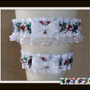 May include: A pair of white elastic garters featuring a colorful Marvel superhero comic book print. Each garter is adorned with a central white satin bow and a delicate white lace trim along the bottom edge, showcasing various comic characters.