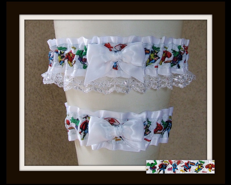 May include: A pair of white elastic garters featuring a colorful Marvel superhero comic book print. Each garter is adorned with a central white satin bow and a delicate white lace trim along the bottom edge, showcasing various comic characters.