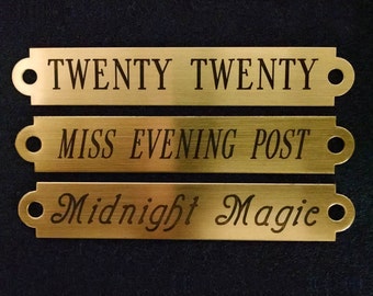 May include: Three gold-colored metal nameplates with rounded edges and holes at the ends. The top plate reads "TWENTY TWENTY", the middle plate reads "MISS EVENING POST", and the bottom plate reads "Midnight Magic" in a cursive font.
