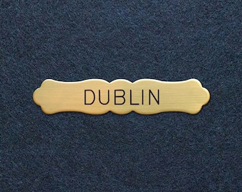 May include: A gold-colored metal sign with the word "DUBLIN" engraved in black lettering.