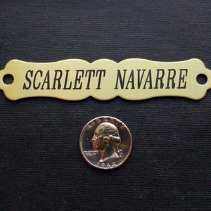 May include: A brass nameplate with a scalloped edge and two holes. The nameplate is engraved with the name "SCARLETT NAVARRE".