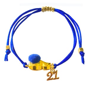 May include: A blue string bracelet with a gold charm shaped like a shoe with a blue pom-pom on top. The charm also has the number "21" hanging from it.