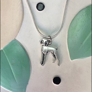 May include: A silver necklace with a small silver dog charm. The dog is standing on all four legs and has a short tail.