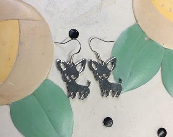 May include: A pair of silver dangle earrings featuring a silhouette of a chihuahua dog.
