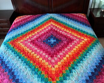 May include: A colorful quilt with a diamond pattern in shades of blue, green, yellow, orange, red, and purple. The quilt is made of squares and has a quilted design.