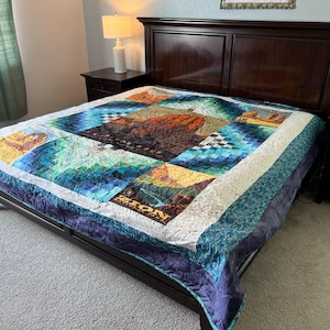 May include: A king-sized bed with a dark wood headboard and a colorful quilt featuring a patchwork design with images of national parks. The quilt has a blue, green, and white color scheme with a white border. The quilt features the word "Zion" in a white font.