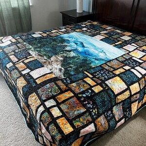 May include: A colorful quilt with a central image of a waterfall and surrounding patchwork squares. The quilt features shades of blue, green, orange, and black. The bedspread is on a dark wood bed frame.