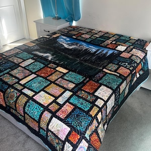 May include: A colorful quilt with a mountain scene in the center. The quilt features a patchwork design with various patterns and colors, including teal, orange, and black. The quilt is displayed on a bed, showcasing its size and design.