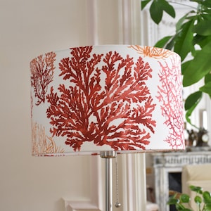 May include: A lampshade featuring a coral reef design in shades of red and orange against a white background. The lampshade is mounted on a silver lamp base. The design evokes a coastal theme, suitable for home decor.