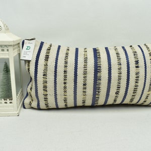 May include: A long, rectangular pillow with a white and blue striped pattern. The pillow is made of a woven fabric with a slightly textured surface.