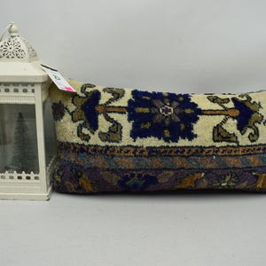 May include: A long, rectangular pillow with a cream-colored background and a blue, brown, and green floral pattern. The pillow is made of a soft, woven fabric.