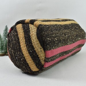 May include: A cylindrical pillow with a black, beige, and pink striped pattern. The pillow is made of a woven fabric and has a slightly textured surface.