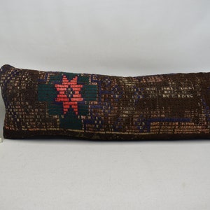 May include: A long, rectangular brown pillow with a colorful geometric pattern. The pattern features a large, red star in the center.