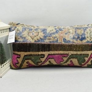 May include: A rectangular cushion with a colourful patterned design. The cushion is made from a woven fabric with a variety of colours, including blue, green, pink, and brown. The cushion is sitting on a white surface.