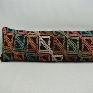 May include: A long, rectangular cushion with a black background and a colourful geometric pattern. The pattern features squares with a variety of colours, including orange, green, blue, and pink.