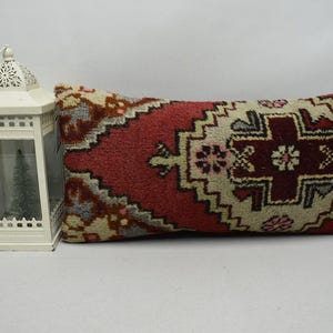 May include: A long, rectangular pillow with a red, white, and beige patterned design. The pillow is made of a soft, woven fabric and has a traditional, geometric pattern.