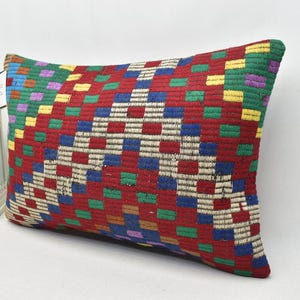 May include: A rectangular cushion with a colourful geometric pattern. The cushion is made of woven fabric and features a variety of colours, including red, green, blue, yellow, and purple.