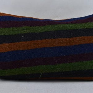 May include: A rectangular cushion featuring bold, horizontal stripes in a mix of colours including brown, green, blue, and black. The fabric appears textured, possibly woven. The colour palette creates a rustic and natural aesthetic.