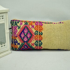 May include: A beige rectangular pillow with a colorful embroidered design. The design features a diamond shape with floral motifs in shades of pink, green, blue, and orange.