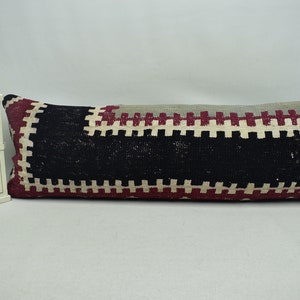 May include: A long, rectangular pillow with a black, white, and burgundy geometric pattern. The pillow is made of woven fabric and has a fringed edge.