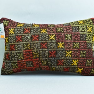 May include: A rectangular cushion with a brown, red, yellow and green geometric pattern. The cushion is made of woven fabric and has a fringed edge.