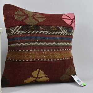May include: A red, brown, and green patterned throw pillow with a woven design. The pillow has a pink flower design on one side and a geometric pattern on the other side.