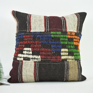 May include: A square cushion with a brown, white and burgundy striped pattern. The centre of the cushion features a colourful geometric design with red, blue, green and orange threads.
