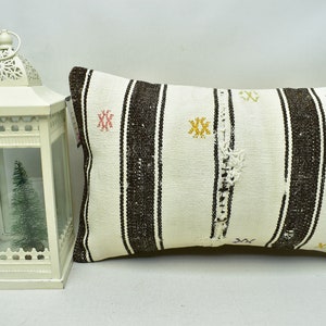 May include: A white and brown striped pillow with embroidered details. The pillow is made of woven fabric and has a rustic, handmade look.