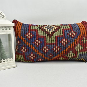 May include: A rectangular cushion with a colourful geometric pattern in shades of red, blue, green, and orange. The cushion is made of woven fabric and has a fringed edge.