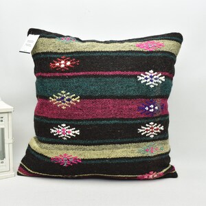 May include: A black, green, pink and white striped cushion with a geometric pattern. The cushion is made of woven fabric and has a fringed edge.