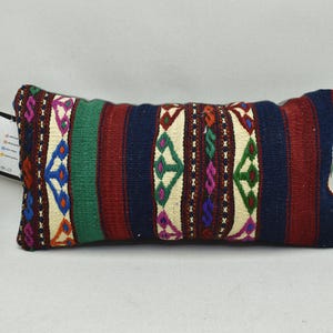 May include: A rectangular cushion with a colourful geometric pattern in shades of red, blue, green, and white. The cushion is made of woven fabric and has a fringed edge.