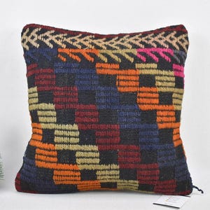 May include: A colourful, geometric patterned throw pillow with a black background. The pillow is made of woven fabric and has a fringe detail.