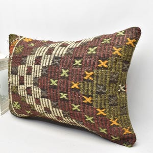 May include: A rectangular pillow with a brown, green, and orange geometric pattern. The pillow is made of woven fabric and has a fringed edge.