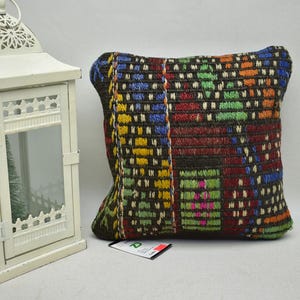 May include: A colourful, geometric patterned cushion with a dark brown background. The cushion is made of woven fabric and has a variety of colours, including red, blue, green, yellow, and white.