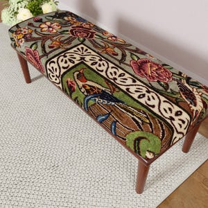 Puede incluir: Banco rectangular con un estampado floral y de p&aacute;jaros en la parte superior acolchada. El dise&ntilde;o presenta rosas burdeos, hojas verdes y un motivo central de p&aacute;jaro. El banco tiene cuatro patas de madera.