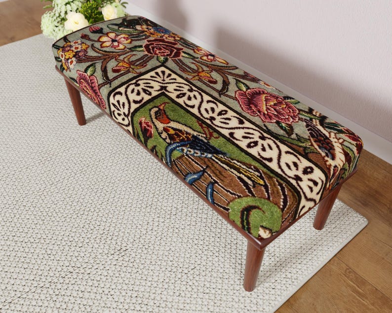 Puede incluir: Banco rectangular con un estampado floral y de p&aacute;jaros en la parte superior acolchada. El dise&ntilde;o presenta rosas burdeos, hojas verdes y un motivo central de p&aacute;jaro. El banco tiene cuatro patas de madera.