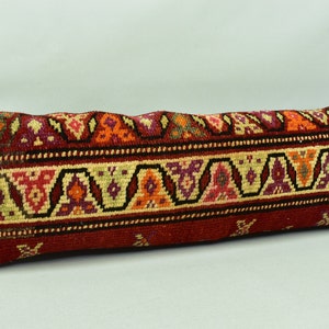 May include: A long, rectangular cushion with a red background and a colourful geometric pattern. The pattern features a variety of colours, including orange, yellow, green, and purple.