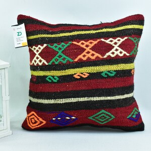 May include: A colorful throw pillow with a geometric pattern in shades of red, black, green, orange, and blue. The pillow is made of woven fabric and has a fringe border.