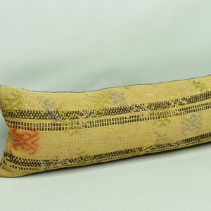 May include: A long, rectangular pillow with a beige background and a striped pattern in black and brown. The pillow has a floral design in shades of purple and green.