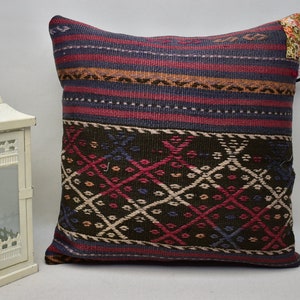 May include: A decorative throw pillow with a colourful geometric pattern in shades of red, blue, green, and brown. The pillow is made of woven fabric and has a fringed edge.
