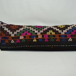 May include: A long, black pillow with a colorful geometric pattern woven into the fabric. The pattern features a variety of colors, including pink, blue, green, yellow, and orange.